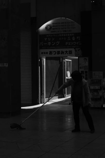 A man cleaning a glass barrier outdoors with a squeegee, surrounded by greenery.